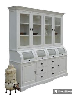 a white china cabinet with glass doors and drawers on the bottom, next to a vase