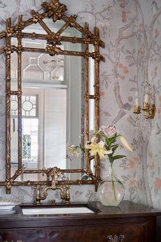 a bathroom sink sitting under a mirror next to a vase with flowers in front of it