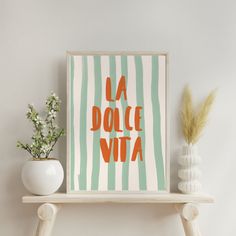 an orange and green striped poster with the words la dolce vita on it next to a white vase