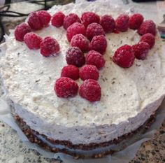 a cake with white frosting and raspberries in the shape of a heart