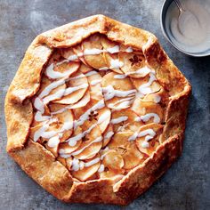 an apple pie with white icing on a table next to a cup of milk