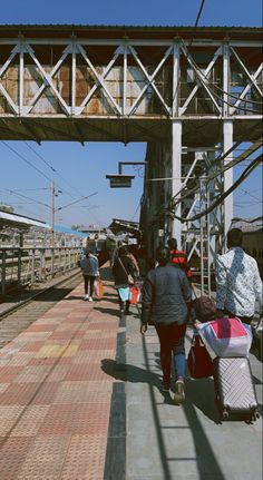 people are walking down the train tracks with suitcases and luggage on their back as they walk under an overpass