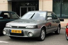 a silver car parked in front of a brick building next to another red car on the street