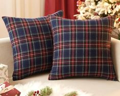 two plaid pillows sitting on top of a white couch next to a christmas tree and presents