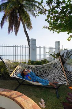 a woman laying in a hammock on the grass next to a palm tree