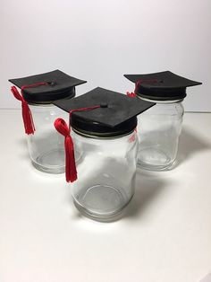 three clear jars with graduation caps and tassels on the lids are lined up