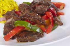 a white plate topped with meat and veggies next to rice on a table