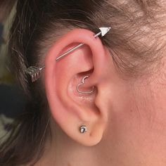 a woman wearing an ear piercing with two silver arrows on the side of her ear