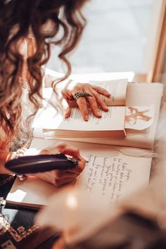 a woman sitting at a table with an open book and pen in her hand while writing on paper