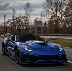 a blue chevrolet sports car driving down the road with trees in the background and clouds in the sky