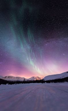 the sky is filled with purple and green lights as the sun sets in the distance