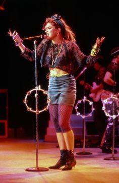 a woman standing in front of microphones on stage with other people behind her and lights around her