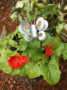 a metal butterfly sitting on top of green leaves and red flowers in a potted plant