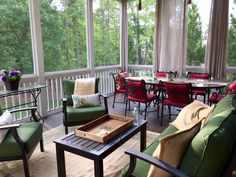 a screened porch with chairs, tables and couches on the deck overlooking trees in the distance