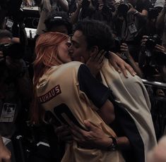 a man and woman are kissing in front of a large group of people with cameras around them