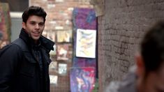 a man standing next to a brick wall with paintings on the walls behind him and people looking at it