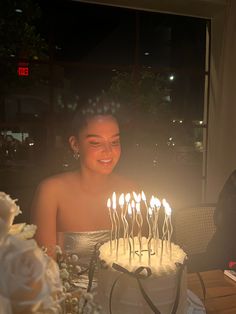 a woman sitting in front of a cake with lit candles