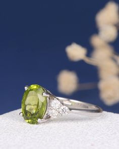 an oval cut peridot and diamond ring on top of a white cloth with flowers in the background