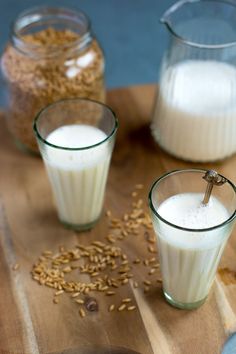 three glasses filled with milk sitting on top of a wooden table next to oats