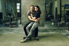 a man and woman sitting on top of each other in front of a room filled with tools