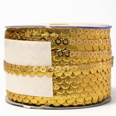 a roll of gold sequinized ribbon with white tags on the side and blue edge