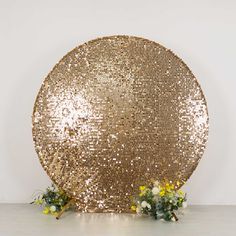 a large gold sequined object sitting on top of a white floor next to flowers