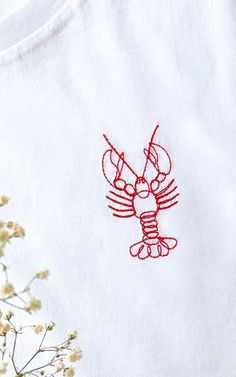 a white t - shirt with a red lobster embroidered on it