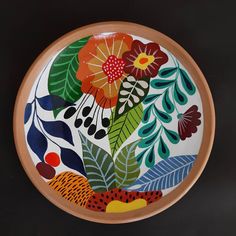 a decorative plate with flowers and leaves painted on the front, sitting on a black surface