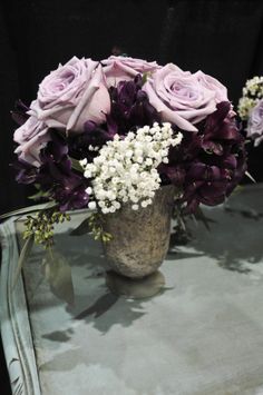 a vase filled with purple and white flowers on top of a glass table next to a mirror