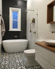 a white bath tub sitting next to a toilet under a bathroom window on top of a black and white tiled floor