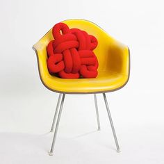 a yellow chair with a red pillow on it's back sitting in front of a white background