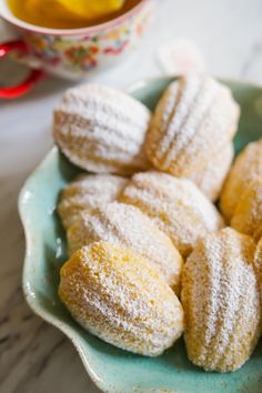 powdered sugar covered donuts on a blue plate next to a cup of tea