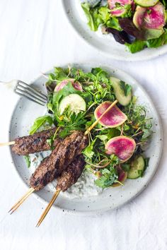 two plates filled with meat and vegetables on top of a white table cloth next to each other