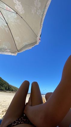 a woman laying on top of a beach under an umbrella