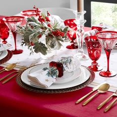 the table is set for christmas dinner with red and white dishes, silverware, and greenery