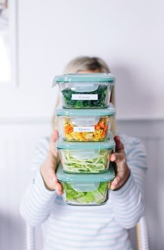 a woman holding three plastic containers filled with food