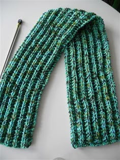 a green knitted scarf next to a knitting needle