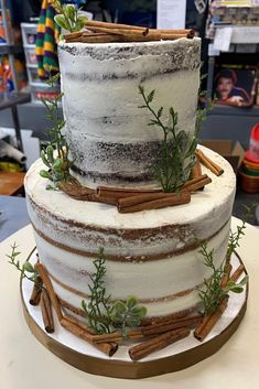 a three tiered cake with cinnamon sticks and greenery on the top, sitting on a table in a store