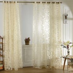 a living room with white walls and curtains on the windowsills, along with a wooden floor