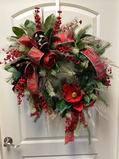 a christmas wreath hanging on the front door with red and green flowers, greenery and poinsettis