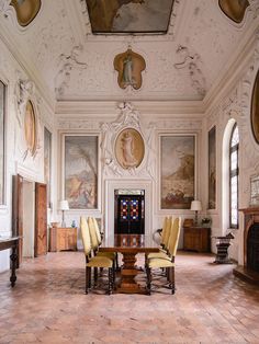 a large room with paintings on the walls and two tables in front of them, along with yellow chairs