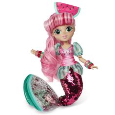 a little mermaid doll with pink hair and green pants, standing next to a watermelon