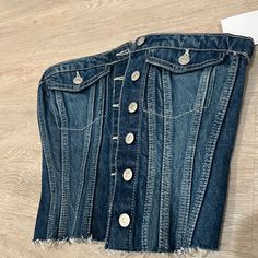 a pair of jeans with buttons on them laying on the floor next to a piece of paper