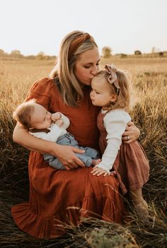 a woman and two children are sitting in the middle of a field with tall grass