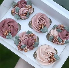 four cupcakes with pink frosting and green leaves on top in a box