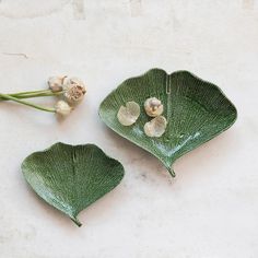 two green leaf shaped dishes sitting on top of a white counter next to some flowers