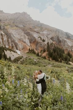 a bride and groom are hugging in the wildflowers at their mountain wedding ceremony