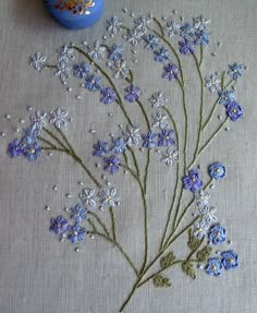 a blue vase sitting next to a white table cloth with flowers embroidered on the side