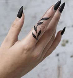 a woman's hand with black nail polish and a leaf tattoo on her finger