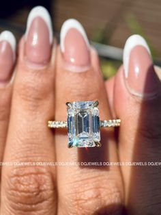 a woman's hand holding a ring with an emerald stone in the center and diamond band around it